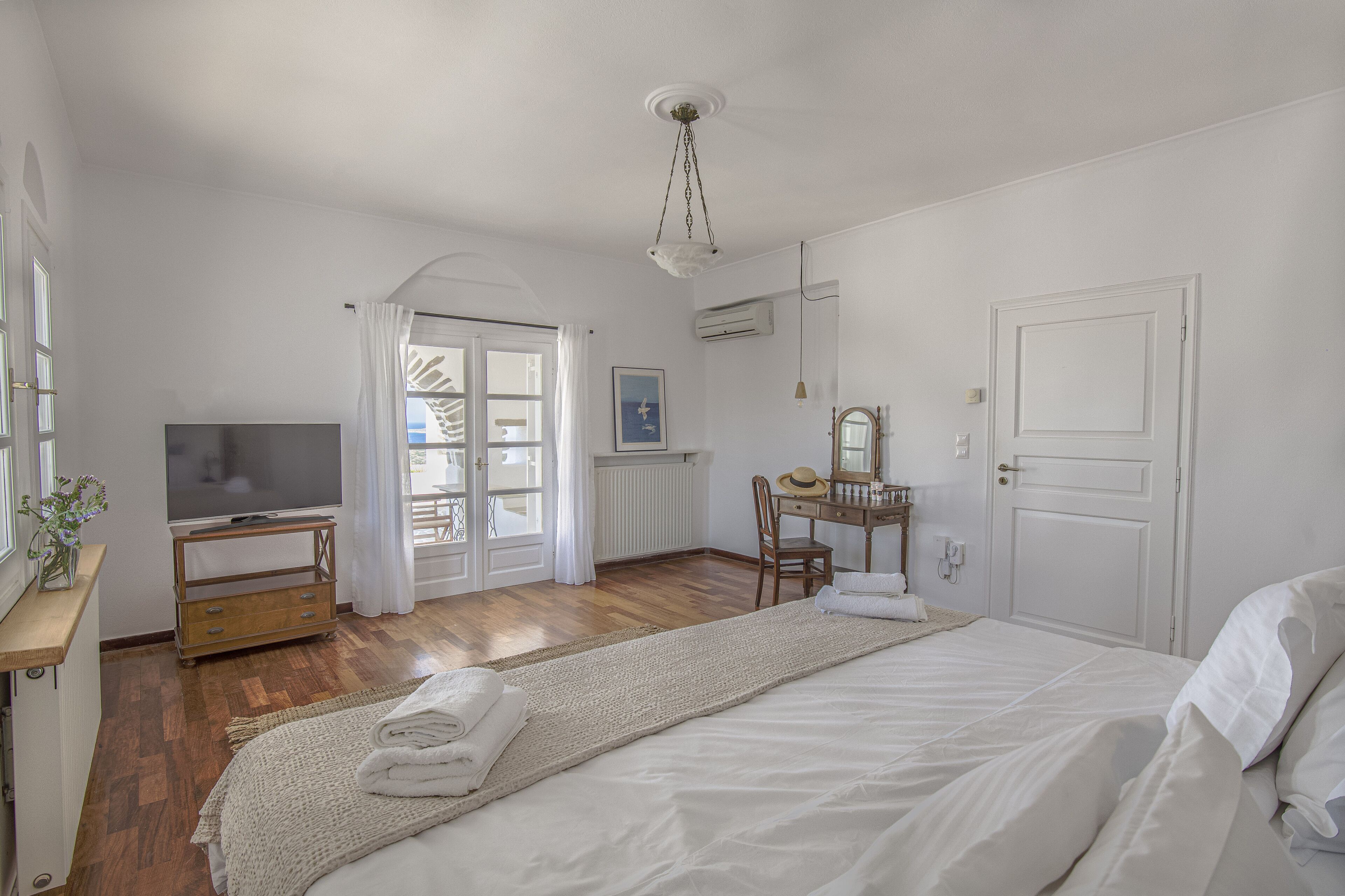 Quarto com cama, televisão, escrivaninha e cadeira.