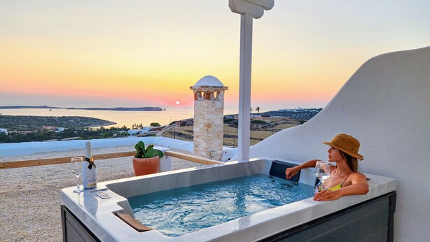 A hot tub with a view of the sunset over the sea, a potted plant, and a bottle of champagne on a balcony. - Anthemion Paros Villas & Suites (Paros)