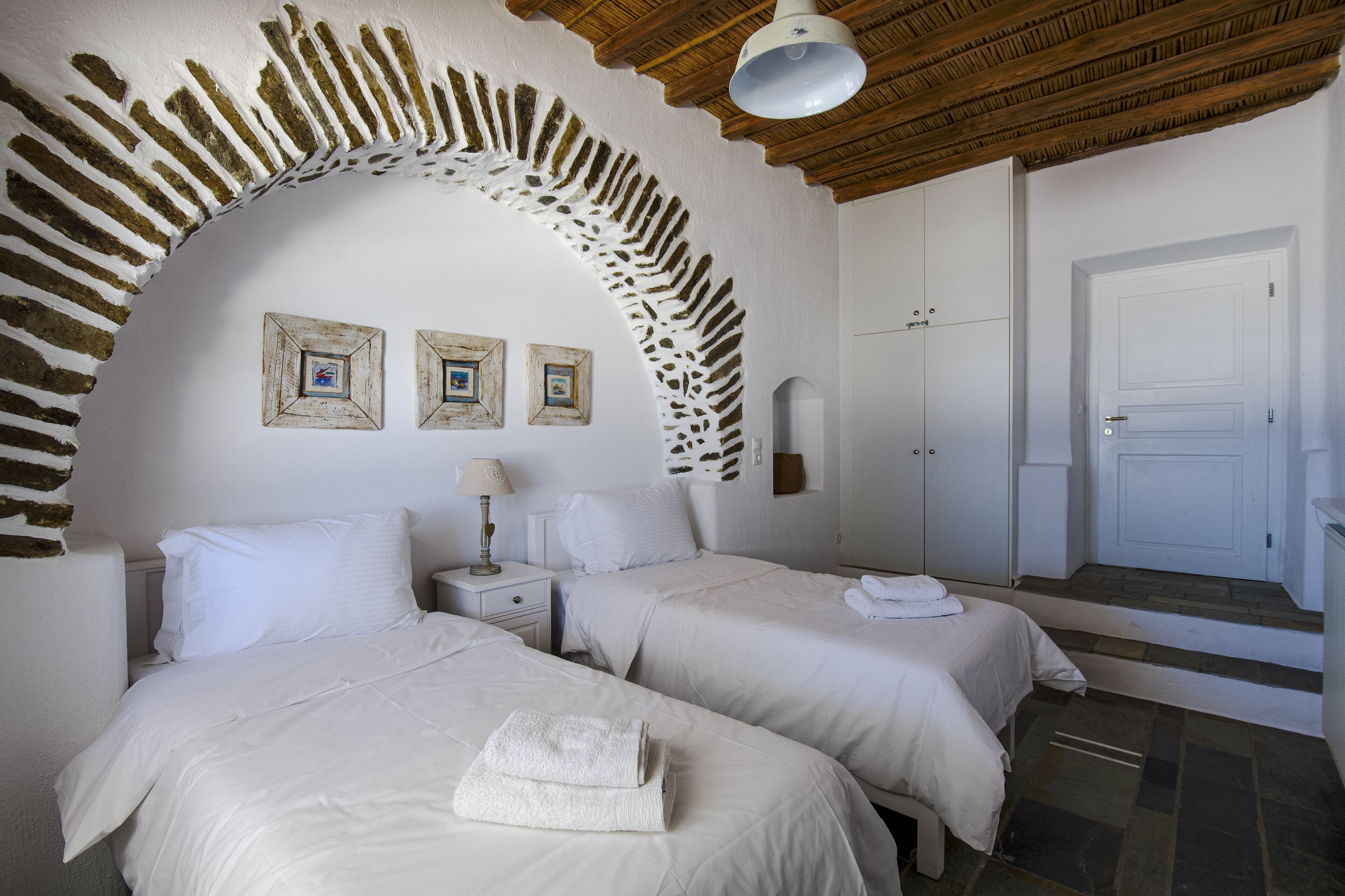 A room with two beds, a white arched doorway, and three framed pictures on the wall.