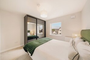 Un dormitorio con cama, espejo, ventana y radiador.