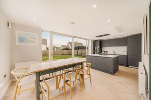 A modern kitchen with a central island, dark cabinets, and a view of the backyard. - New | Family Haven | Walk to Rossnowlagh Beach | Large Garden | Sauna (Rossnowlagh Lower)