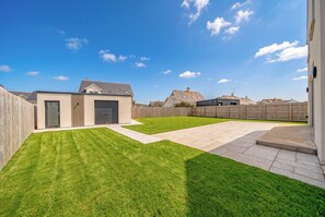 A residential backyard with a well-maintained lawn, a garage, and a wooden fence. - New | Family Haven | Walk to Rossnowlagh Beach | Large Garden |  Sauna (Rossnowlagh Lower)