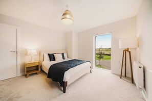 A bedroom with a bed, bedside table, lamp, radiator, and a view of the outdoors. - New | Family Haven | Walk to Rossnowlagh Beach | Large Garden | Sauna (Rossnowlagh Lower)