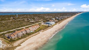 Eine Luftaufnahme einer Küstenlandschaft mit einem langen Sandstrand, blauem Himmel und einem Wasserhochbehälter in der Ferne.