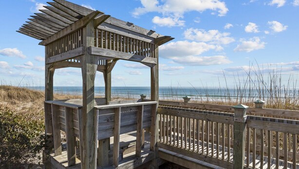 Ein hölzerner Strandpavillon mit geneigtem Dach, gelegen auf einer Holzpromenade mit Blick auf Strand und Meer.