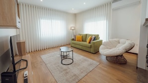 Una sala de estar moderna con un sofá verde, un sillón blanco, una mesa de centro de vidrio y una lámpara de pie.