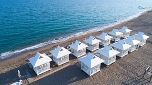 Une rangée de cabanes de plage blanches, avec une plage et l’océan en arrière-plan.