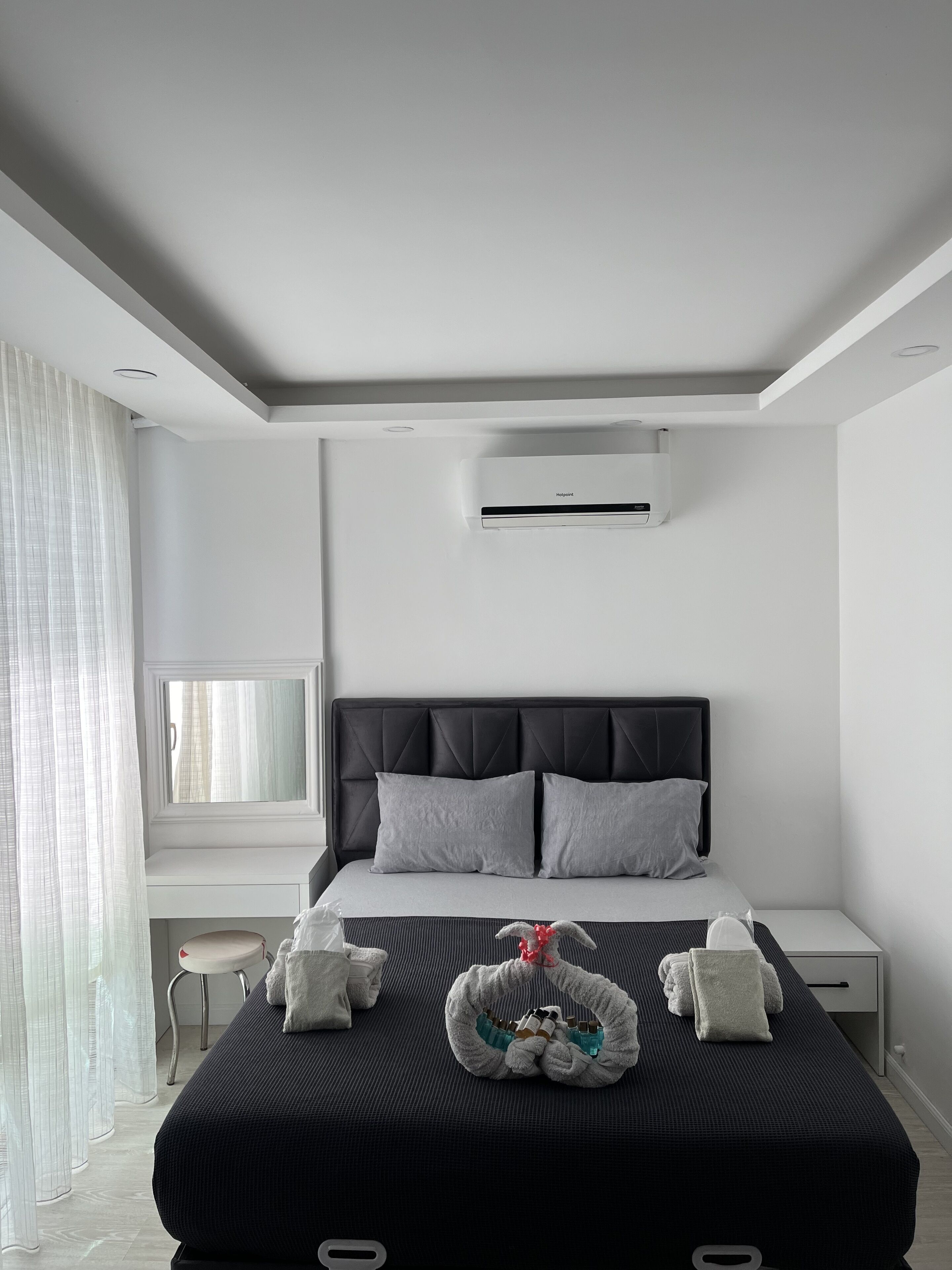 Une chambre d’hôtel moderne avec un grand lit, une table de chevet, un petit bureau et une fenêtre avec des rideaux légers.