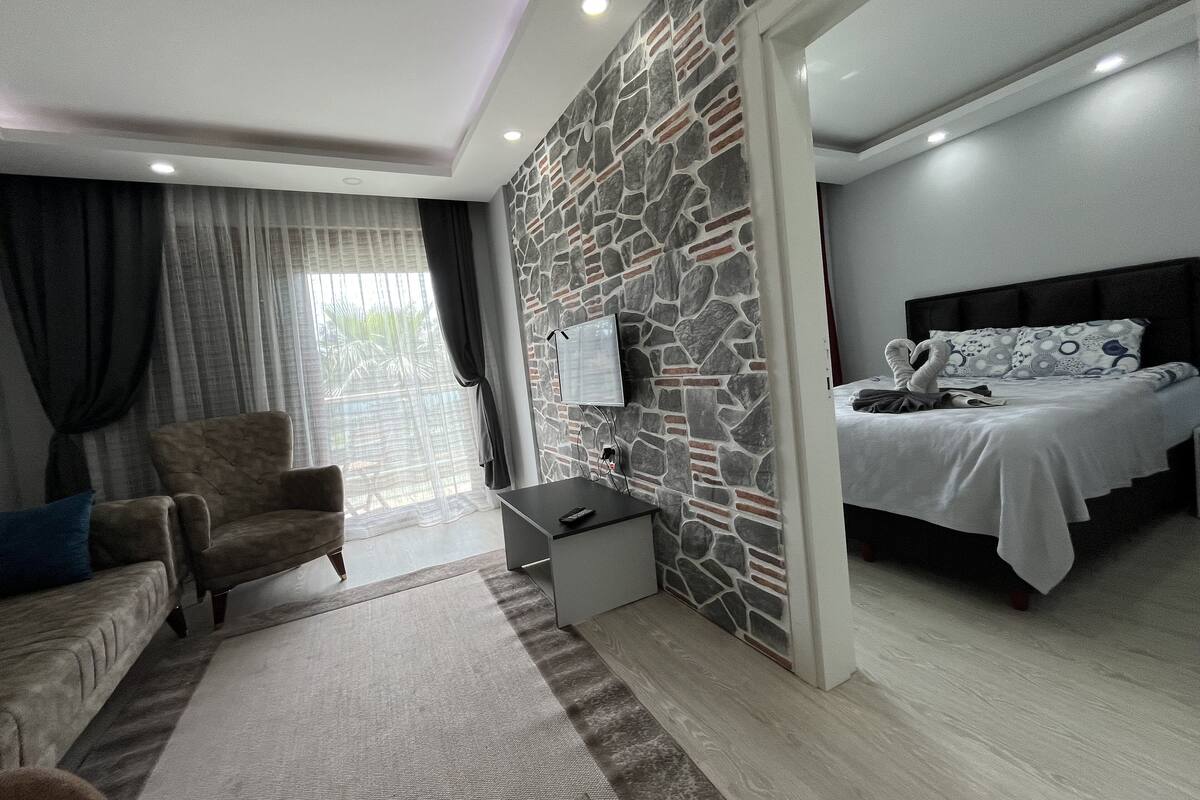 Ein modernes Schlafzimmer mit Steinwand, einem Bett mit gemusterten Betttextilien, einer Couch mit blauem Kissen und einem an der Wand montierten Fernseher.