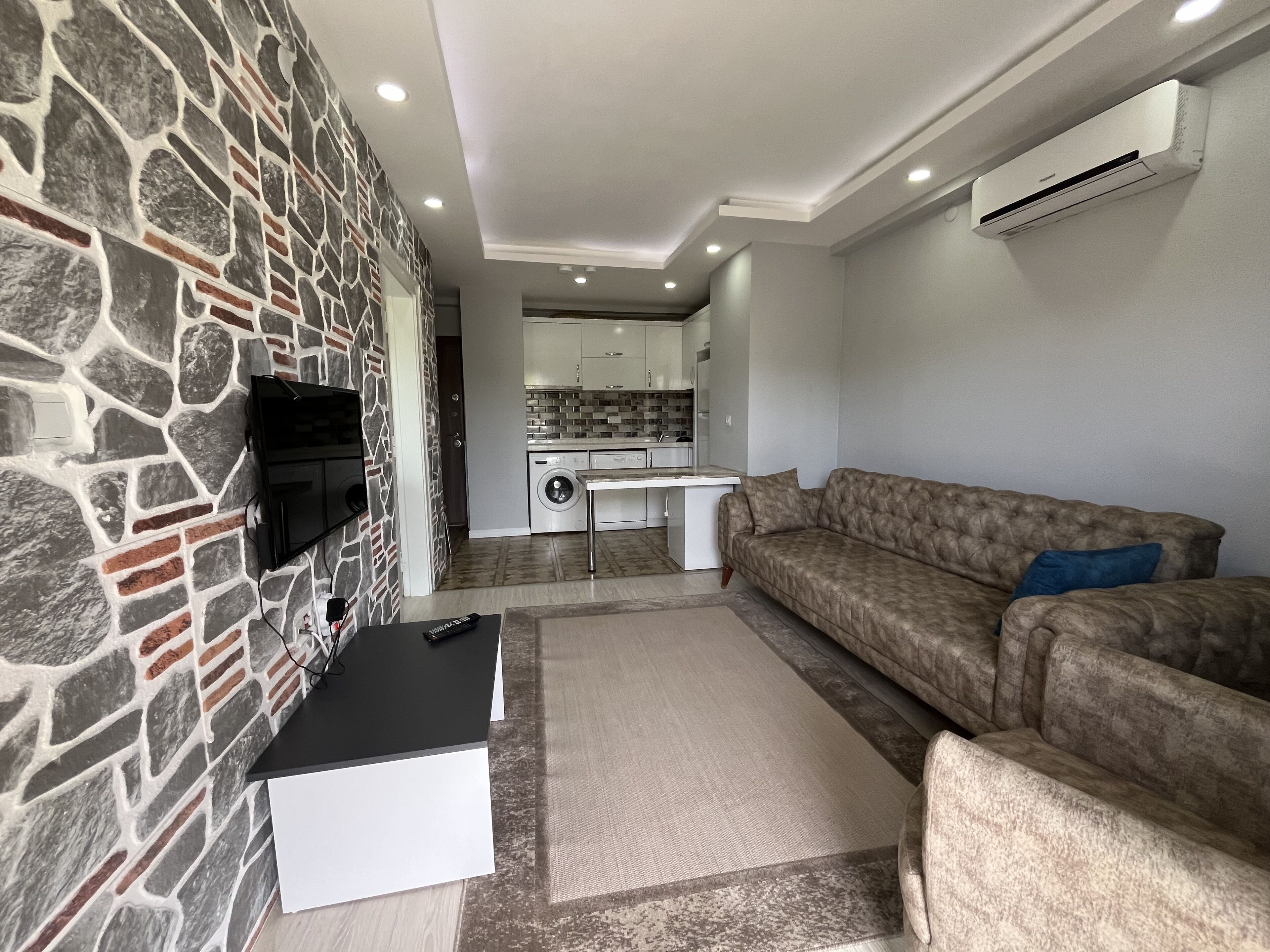 Ein Wohnzimmer mit Steinwand, einer Couch, einem Couchtisch und einem Fernseher.