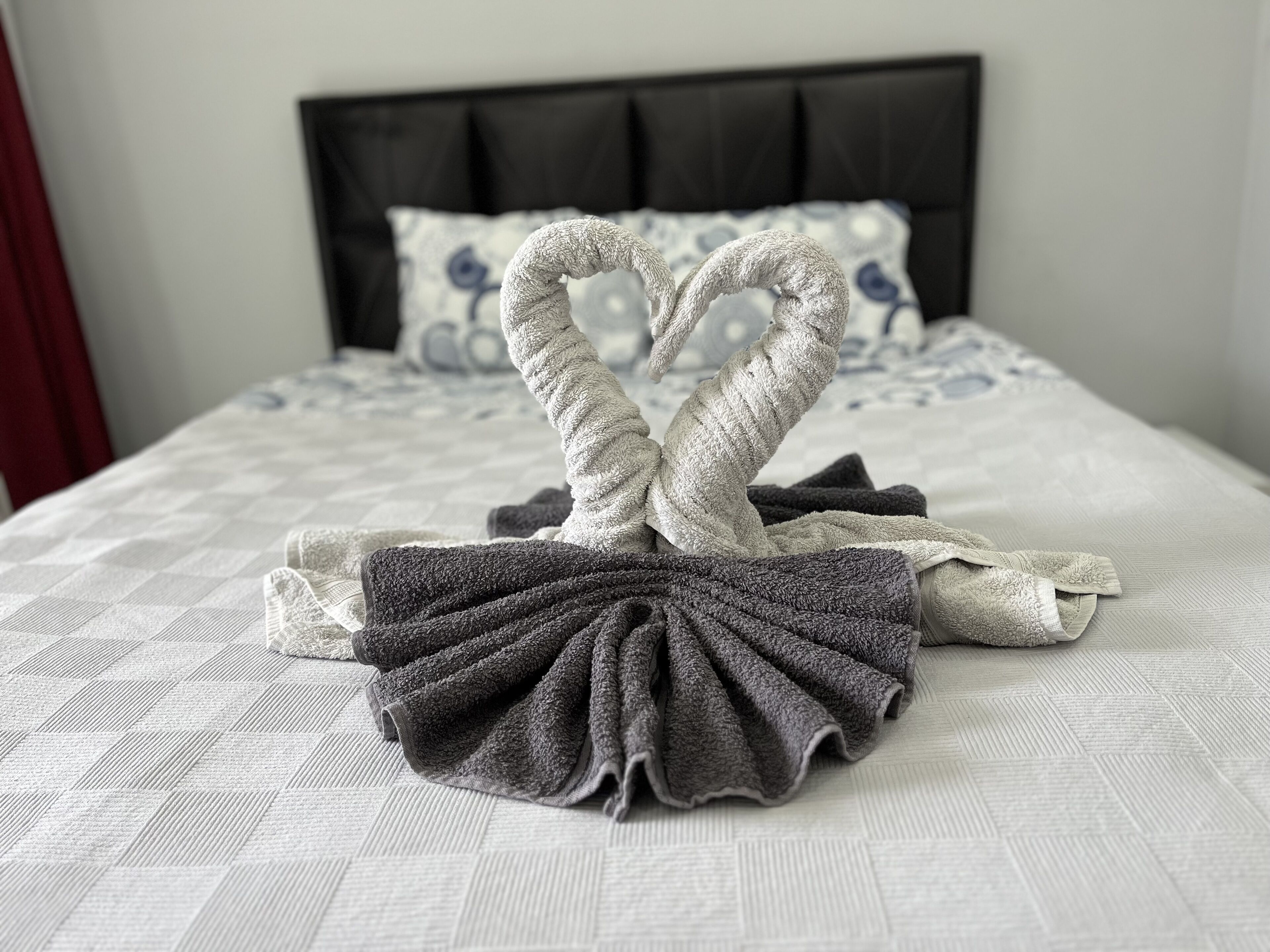 Ein Bett mit weißer Decke und einer Herz-Anordnung aus Handtüchern auf dem Bettbezug.