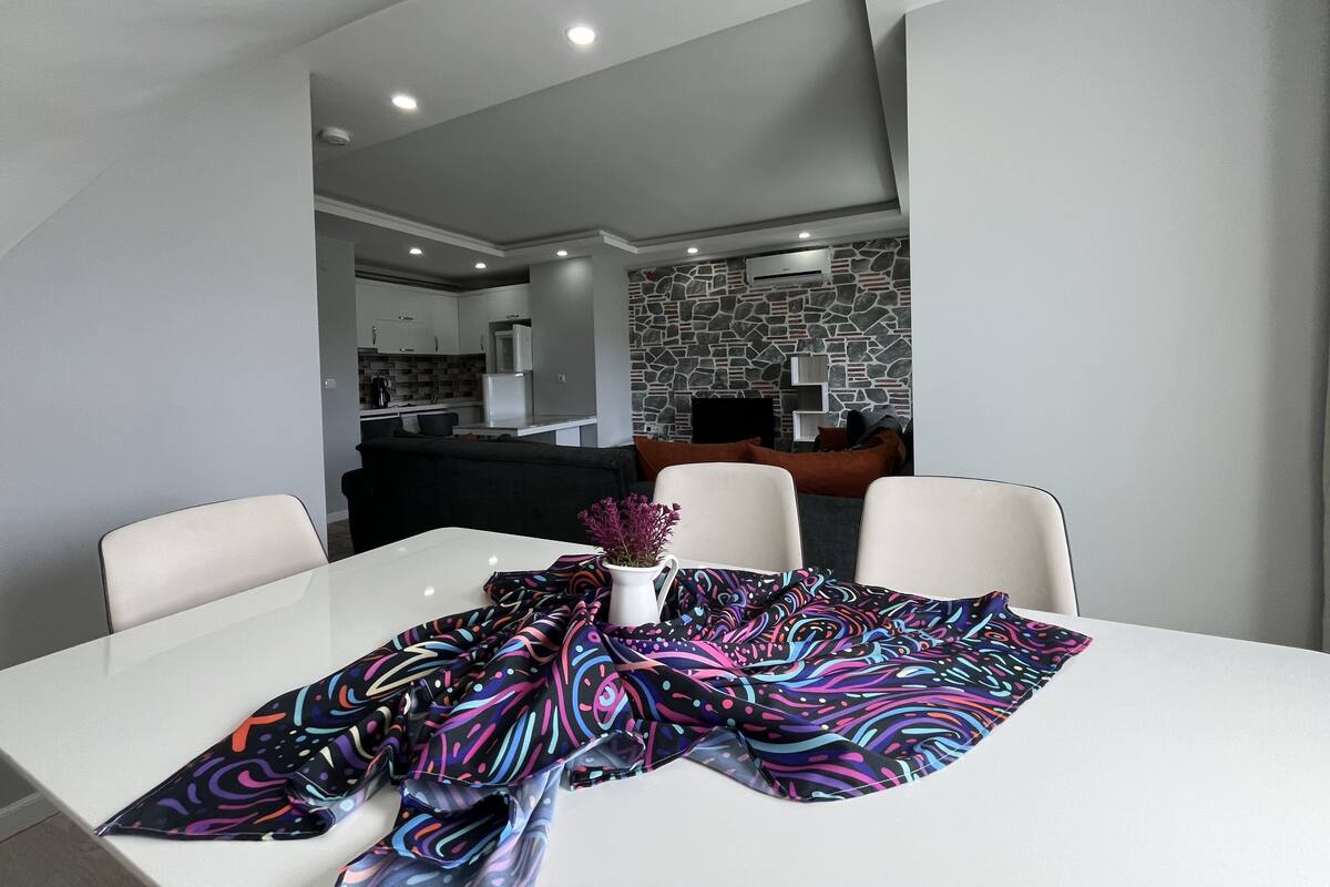 Ein stilvoller Essbereich mit einem weißen Tisch, einer bunten Tischdecke und einer Vase mit Blumen.