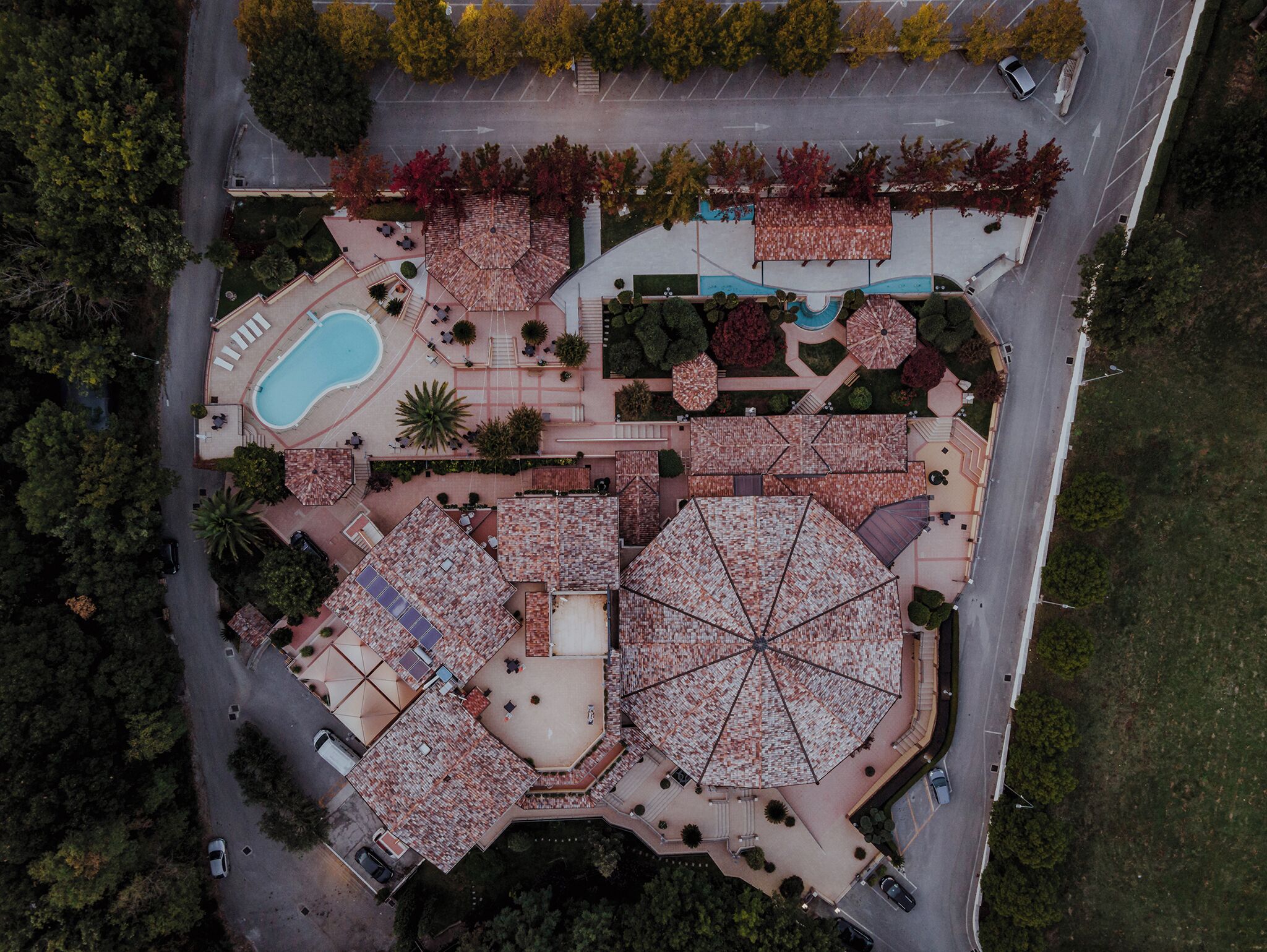 An aerial view of a resort with a swimming pool, multiple outdoor seating areas, and a parking lot.