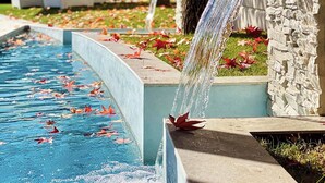 A pool with a waterfall feature, surrounded by stone walls and a garden with autumn leaves. - San Raffaele Hotel Restaurant & Resort (Castelluccio Superiore)