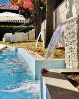 A pool with a waterfall feature, surrounded by stone walls and a garden with autumn leaves.