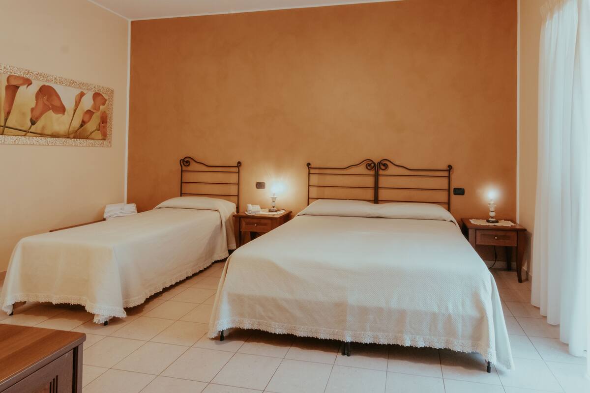 Habitación de hotel con dos camas, un cuadro en la pared y una mesita de noche con lámpara.