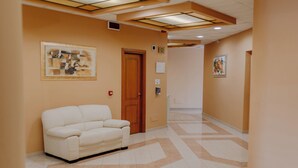 A hallway with a white sofa, a wooden door, and two framed artworks on the walls. - San Raffaele Hotel Restaurant & Resort (Castelluccio Superiore)