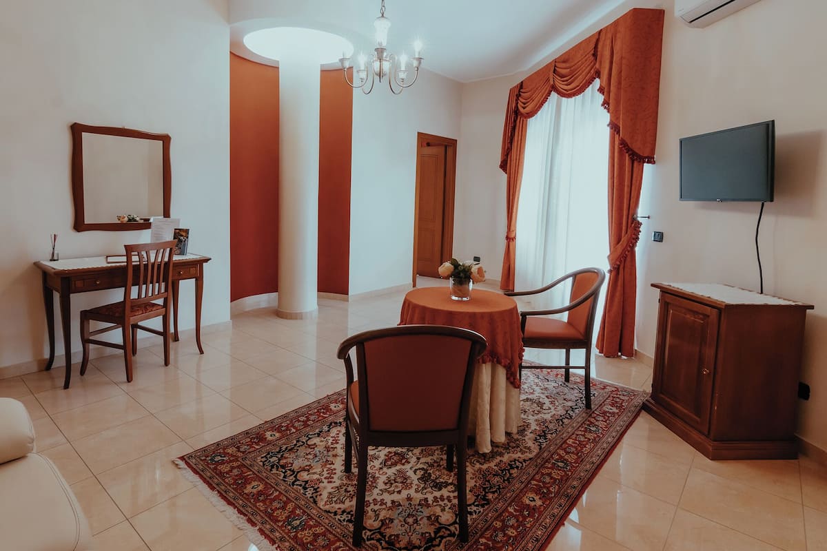 Una sala de estar moderna con comedor, una araña, televisor y un amplio ventanal con cortinas.