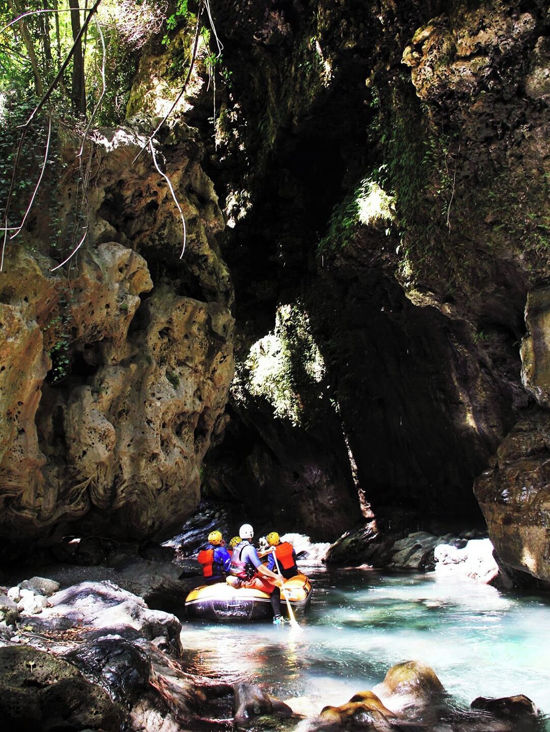 A group of people rafting in a narrow, rocky canyon with clear water.