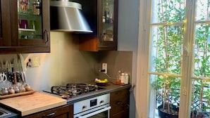 Een keuken met donkere houten kastjes, een roestvrijstalen afzuigkap, een gasfornuis en een oven. Er is een raam met planten buiten.