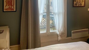 Een slaapkamer met een bed, een raam met gordijnen en twee foto's in lijsten aan de muur.