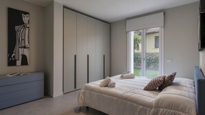 A modern bedroom with a large bed, a wardrobe, a desk, and a window with a view of the outdoors.