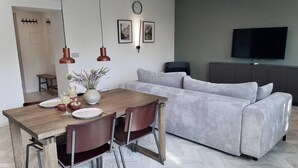 Una sala de estar moderna con un sofá gris, una mesa de comedor de madera y sillas, y un televisor de pantalla plana montado en la pared.