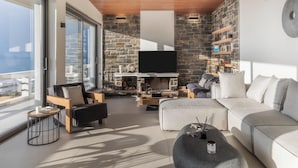 A modern living room with a stone fireplace, a flat-screen TV, and a balcony with a view. - Villa Vel Aegina (Aegina)