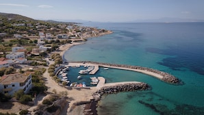 An aerial view of a coastal town with a marina, clear blue waters, and buildings along the shore. - Villa Vel Aegina (Aegina)