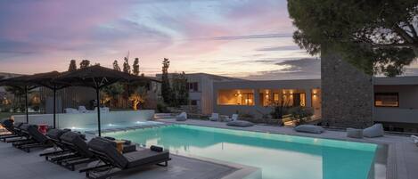 A modern outdoor pool area with lounge chairs and a stone building in the background.