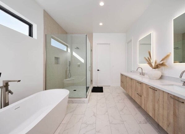 Un baño moderno con ducha de vidrio, una bañera independiente y un tocador con espejo.