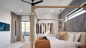 A modern bedroom with a four-poster bed, a geometric-patterned rug, and abstract wall art.