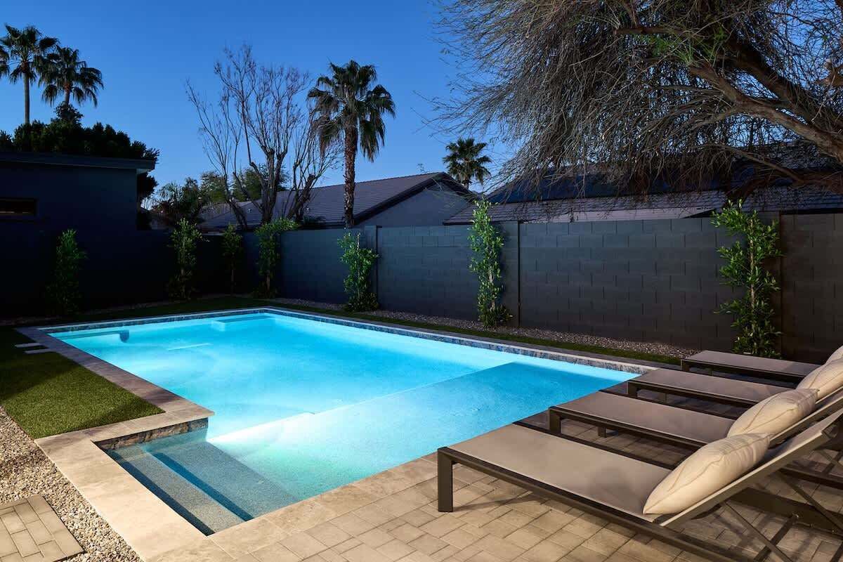 A rectangular swimming pool with lounge chairs and a small grassy area.