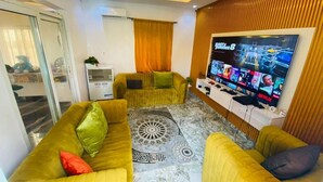 Una sala de estar con un televisor de pantalla plana grande, sofás amarillos, un tapete estampado y un panel de pared de madera.