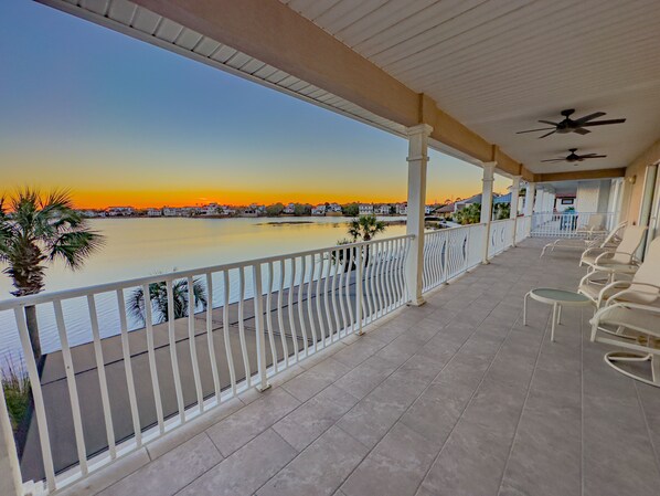 A covered balcony with a view of a sunset over a body of water, white railings, and several chairs. - Beach House, Private Pool, Water view, Sleeps 12, Golf Cart (Destin)