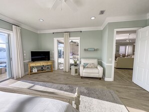 A spacious bedroom with a large bed, a TV on a wooden console, a chair, and a view of the outdoors. - Beach House, Private Pool, Water view, Sleeps 12, Golf Cart (Destin)