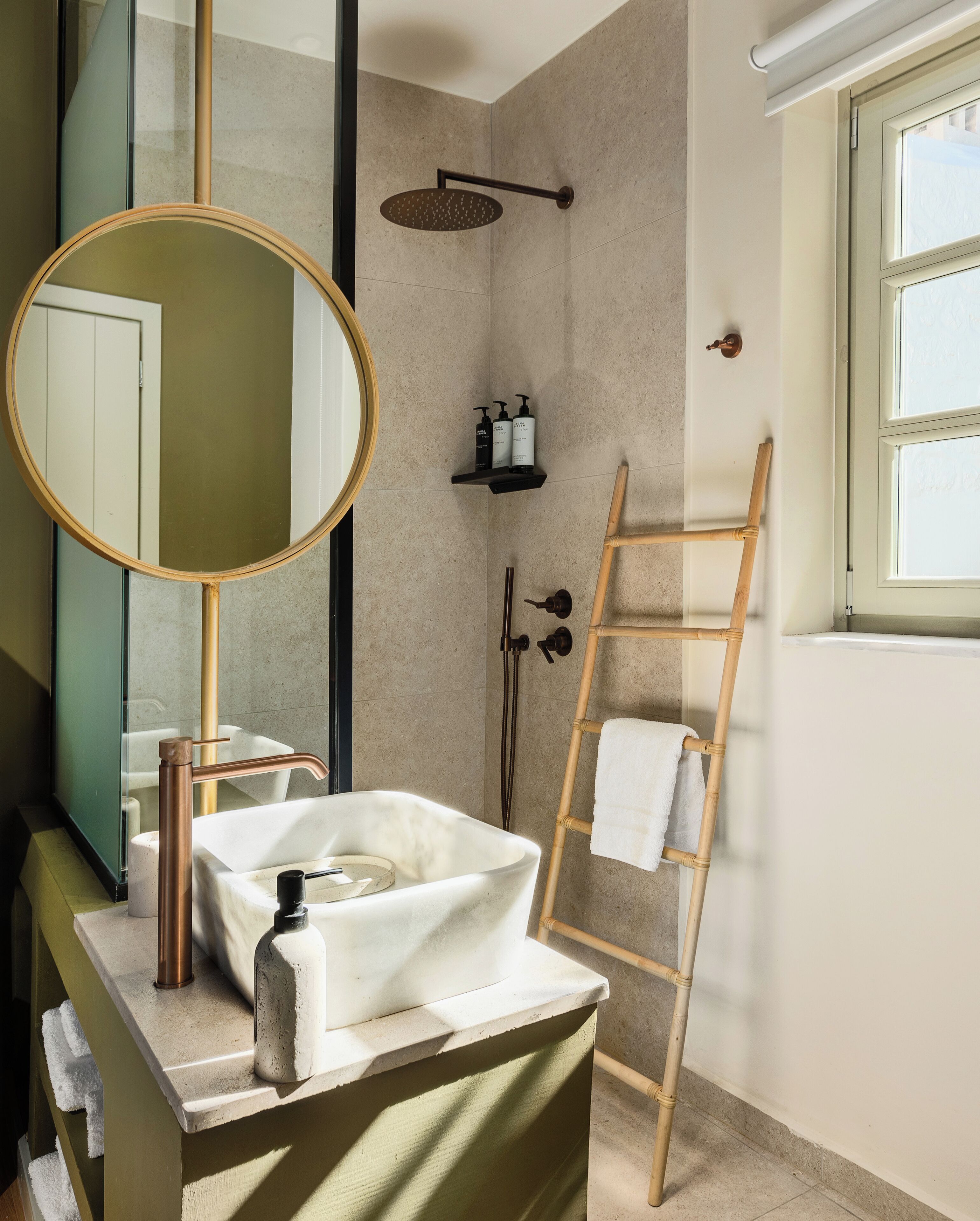 A bathroom with a round mirror, a white sink, a shower, and a wooden ladder.