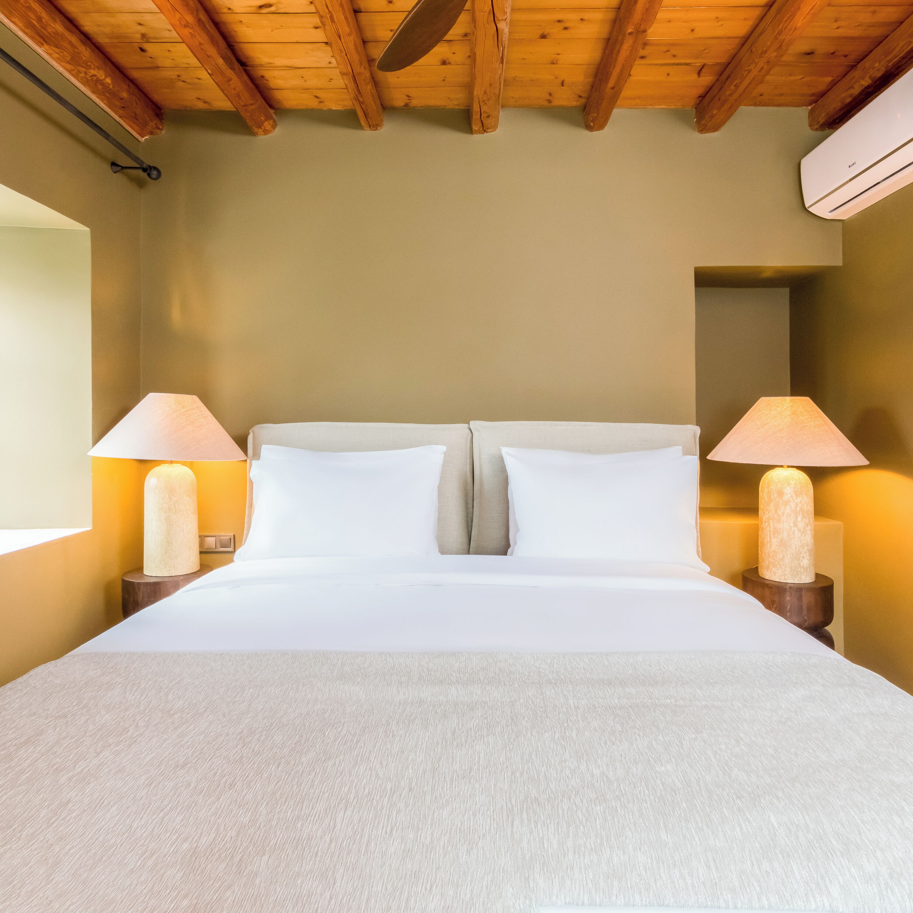Un lit avec du linge de lit blanc, deux lampes de chevet et un plafond en bois.