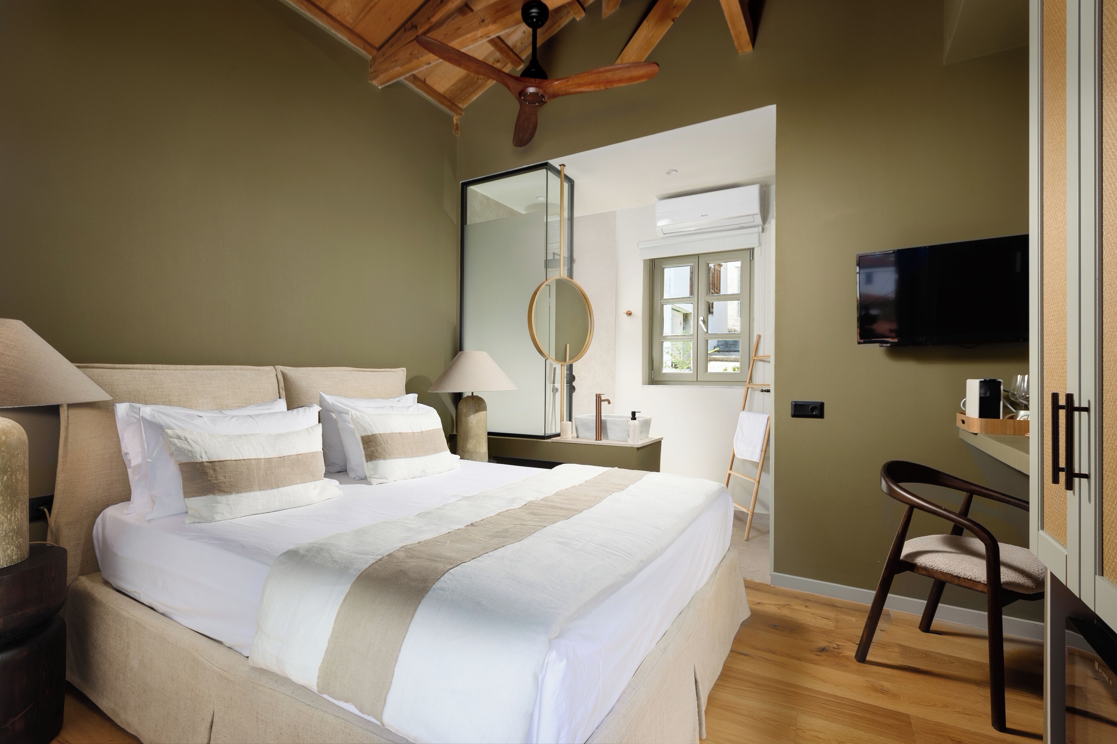 A bedroom with a large bed, a ceiling fan, a TV, and a desk with a chair.