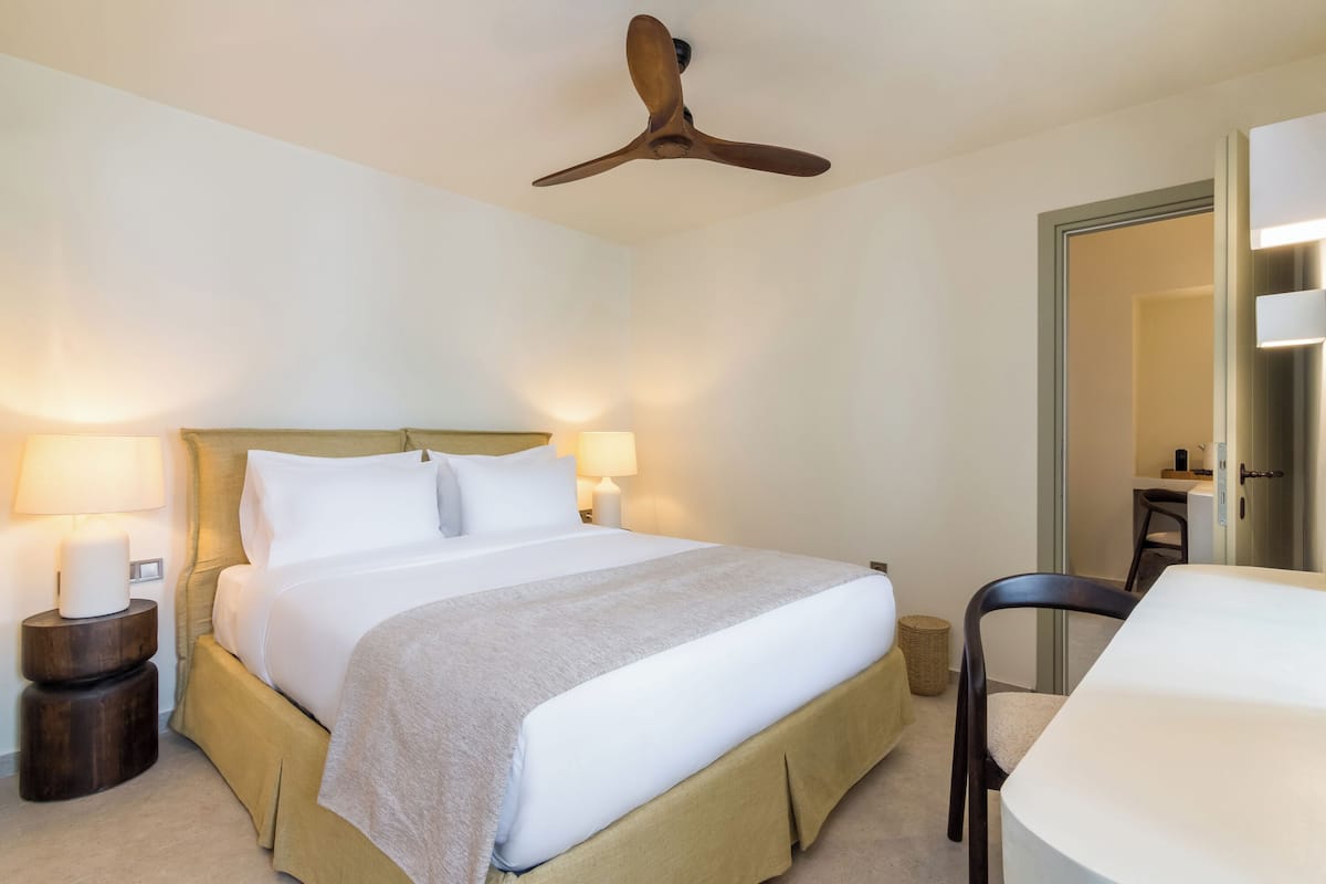 Une chambre d’hôtel avec un lit, des lampes de chevet, un ventilateur de plafond, une chaise et une table.
