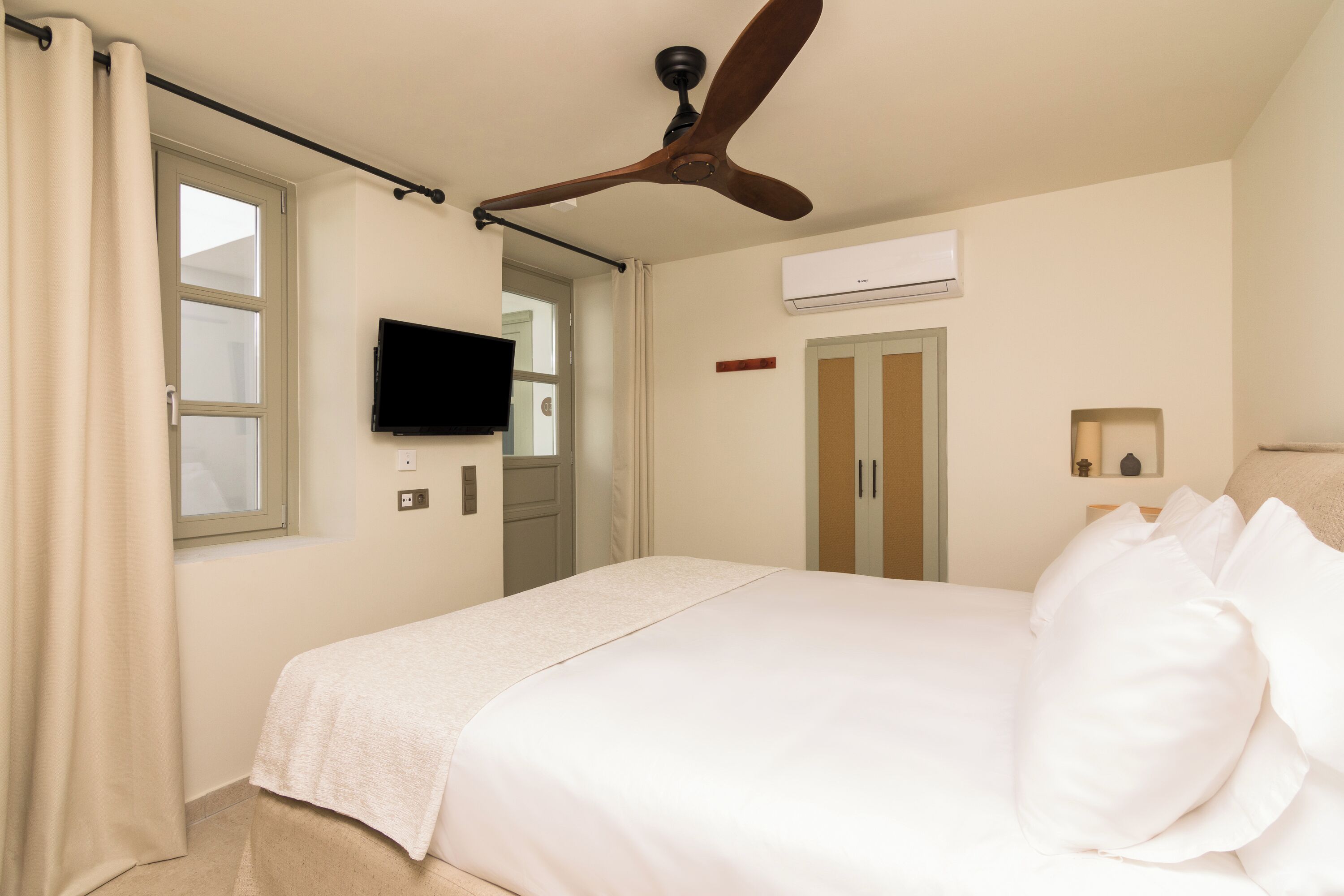 A hotel room with a bed, a ceiling fan, a TV, and an air conditioning unit.