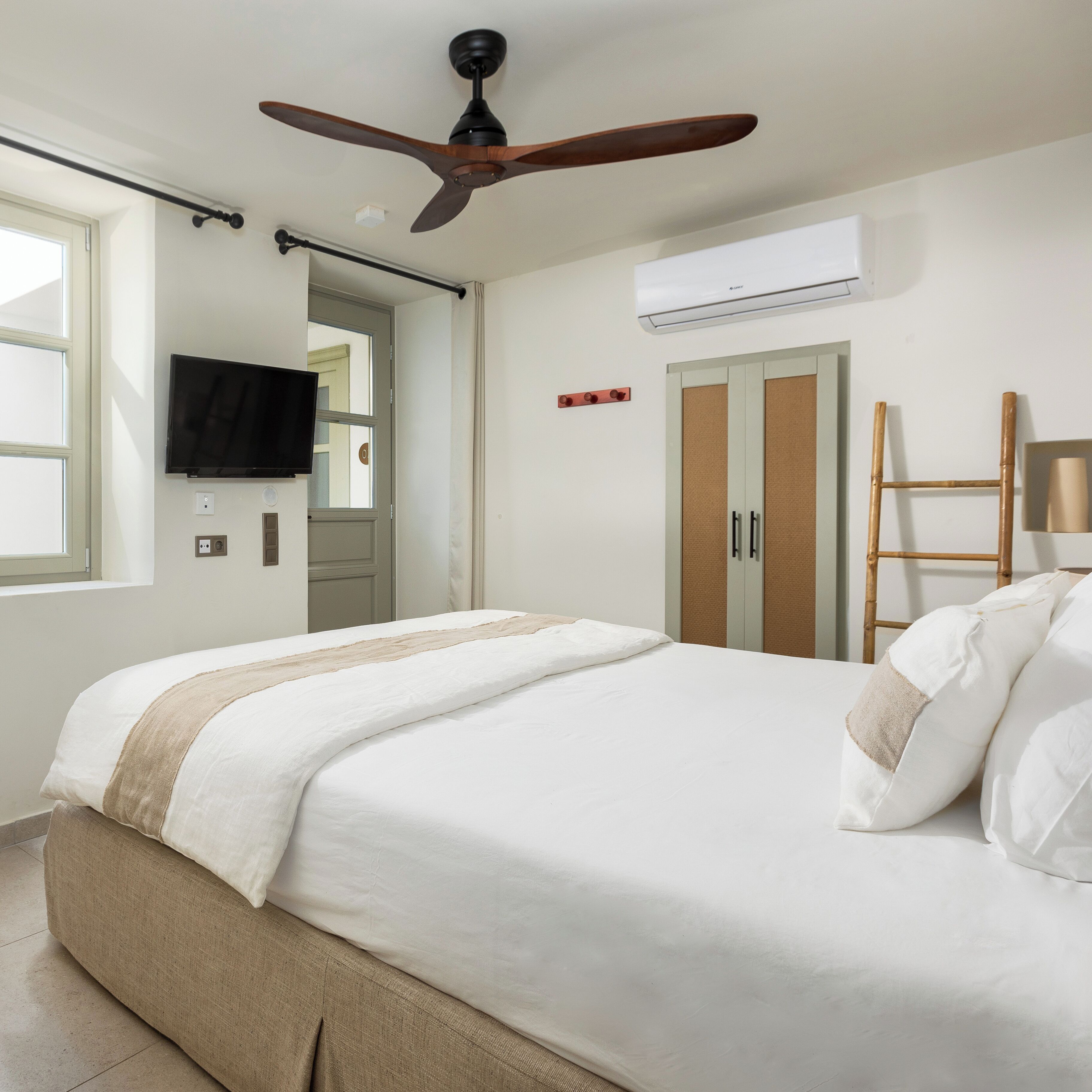 Une chambre à coucher comprenant un lit, un ventilateur de plafond, un appareil de climatisation, une télévision, une armoire et une échelle.