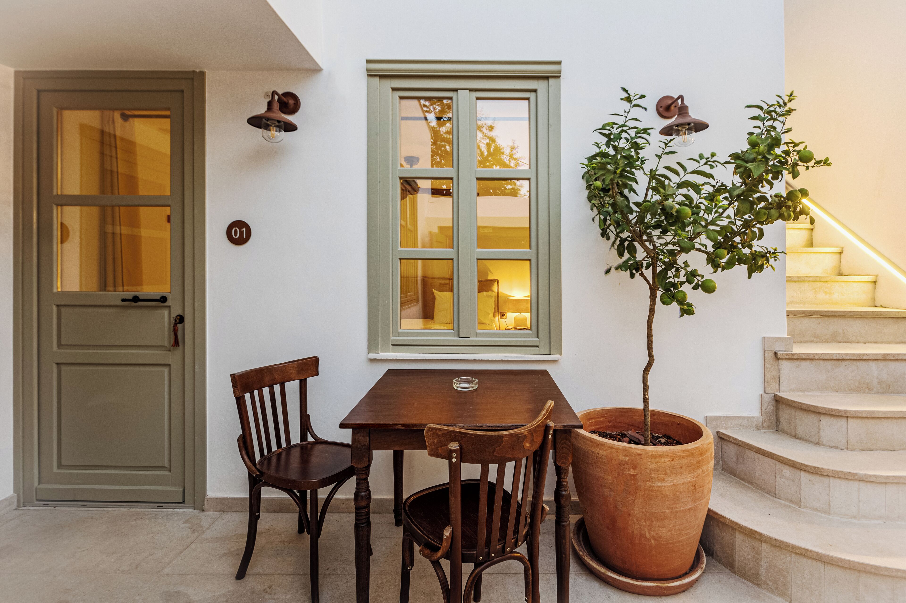 Una mesa de madera con sillas, una planta en maceta, un ventanal con vistas y una escalera.
