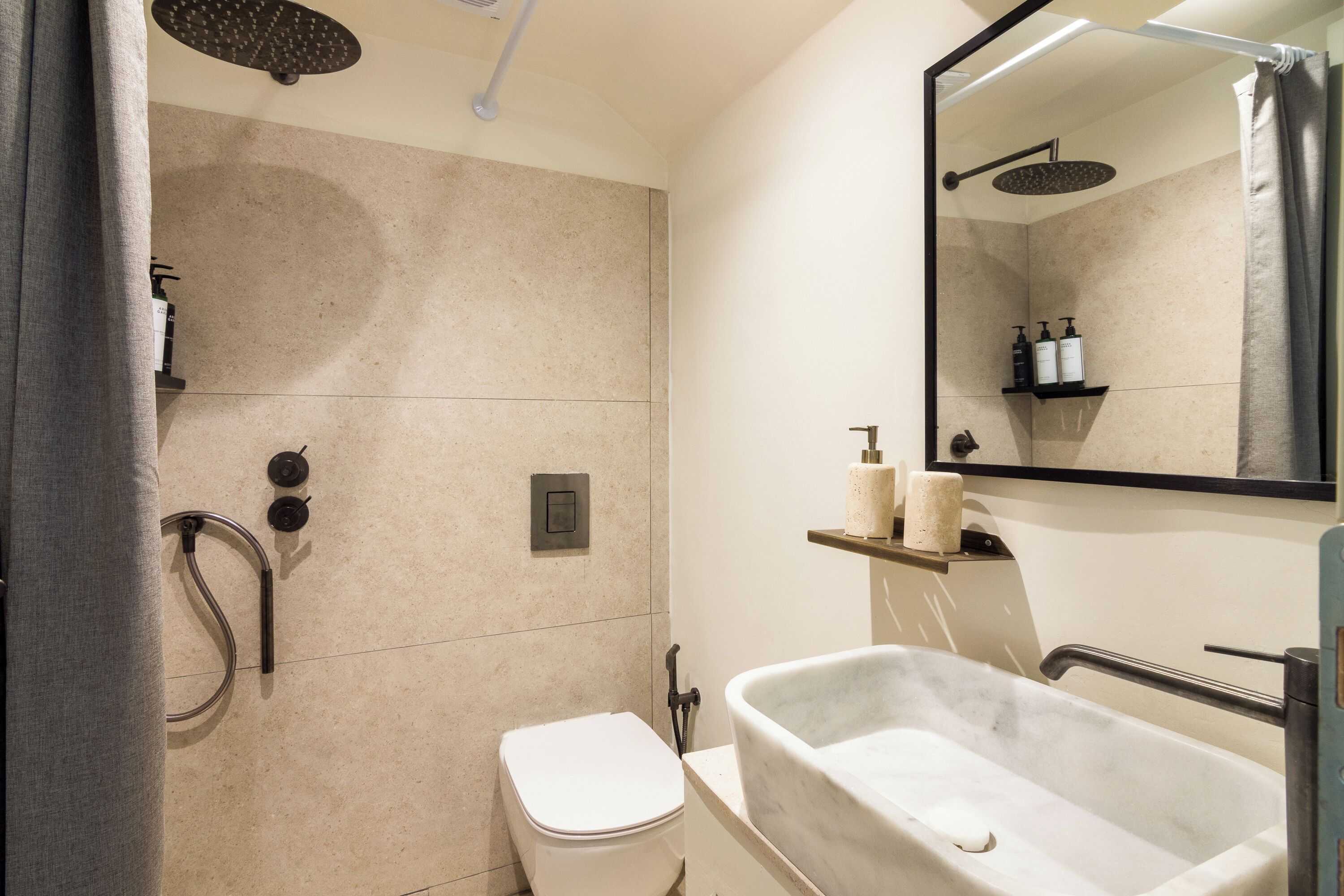 A modern bathroom with a freestanding bathtub, a toilet, a shower with a handheld showerhead, and a mirror above the sink.