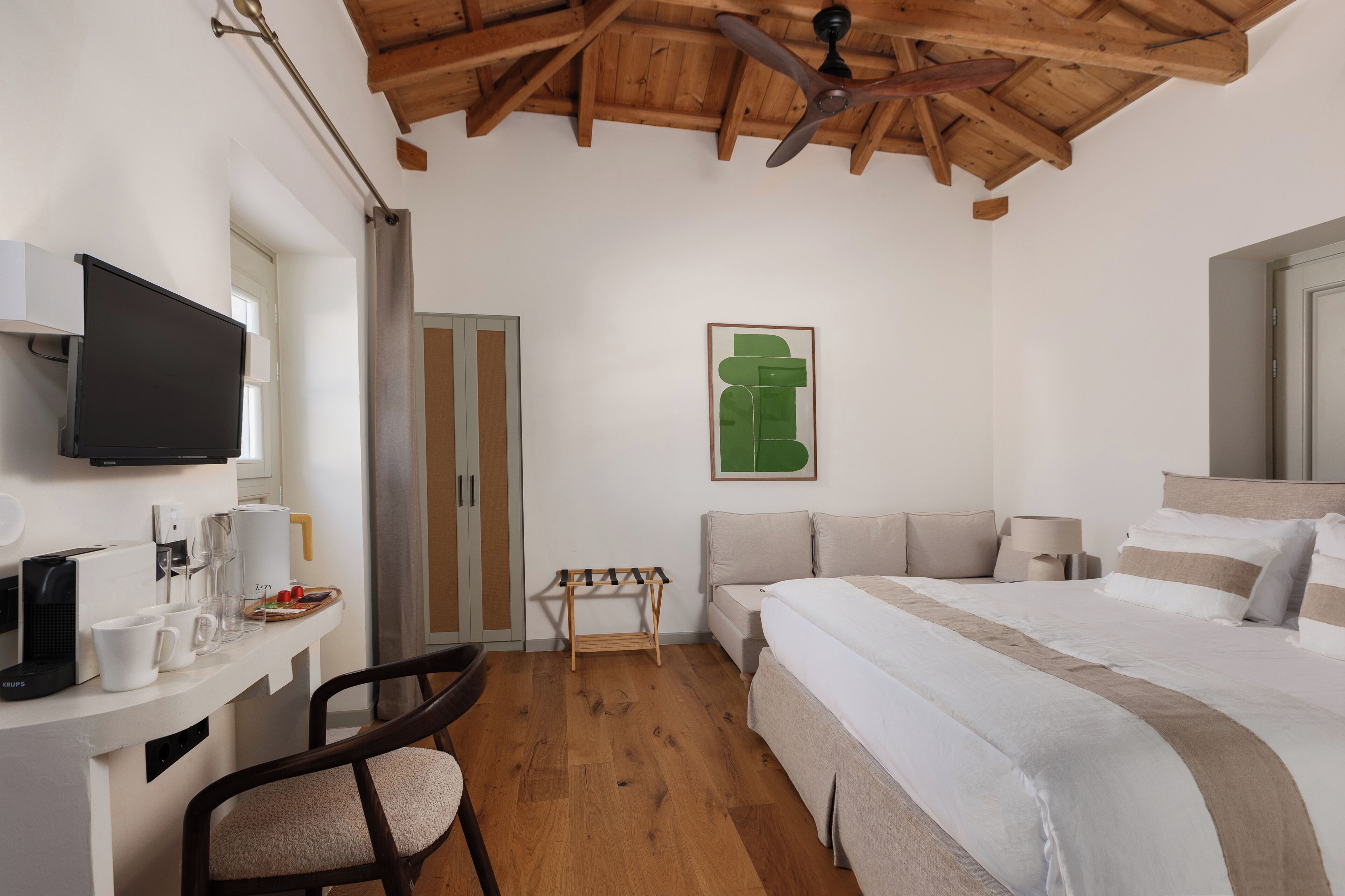 A bedroom with a bed, a desk with a TV, a chair, a sofa, and a ceiling fan.