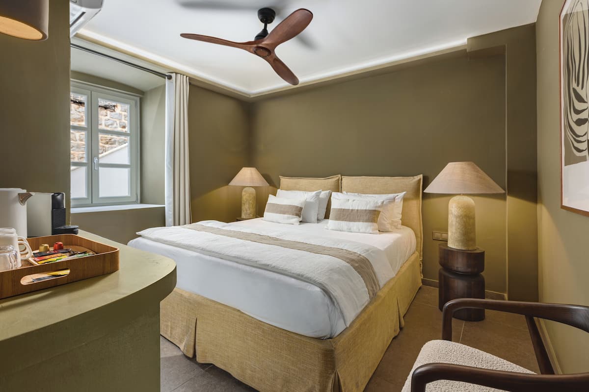 Une chambre à coucher comprenant un lit, des lampes de chevet, un bureau avec un plateau, une chaise et un ventilateur de plafond.