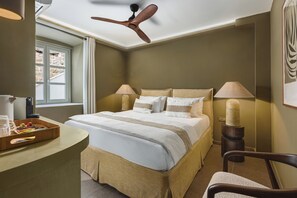 Un dormitorio con una cama, lámparas de noche, un escritorio con bandeja, una silla y un ventilador de techo.