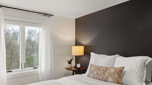 Une chambre à coucher avec un lit, une table de chevet avec une lampe, une horloge et une fenêtre avec des rideaux.