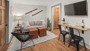 Un salon moderne comprenant un canapé, des poufs, une table basse, un téléviseur et un coin repas avec des chaises et une table.