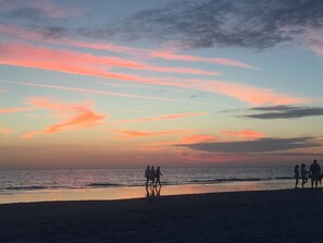 Eine Strandansicht mit Sonnenuntergang, Silhouetten von Menschen, die am Ufer entlanggehen.